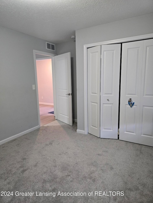 unfurnished bedroom with light carpet, a closet, and a textured ceiling