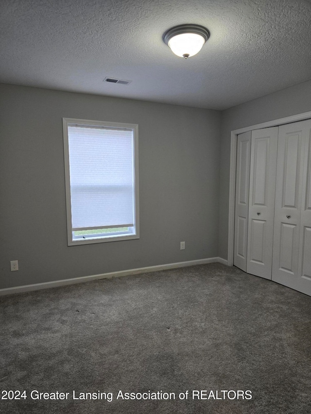 unfurnished bedroom featuring dark colored carpet, a textured ceiling, and a closet