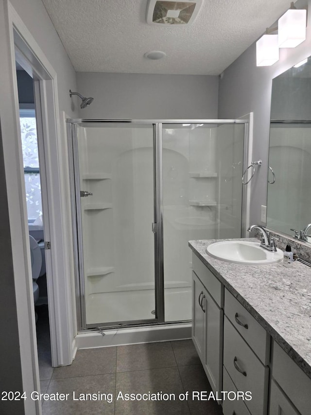 bathroom with vanity, an enclosed shower, a textured ceiling, and tile patterned flooring