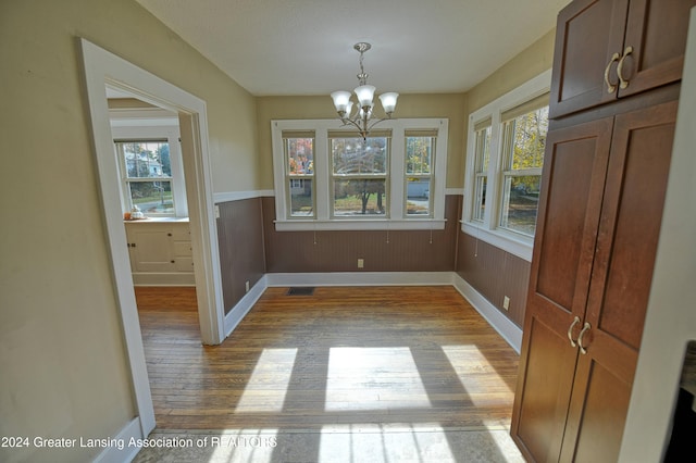 unfurnished dining area featuring wooden walls, a notable chandelier, and light wood-type flooring