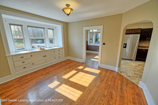 520 W St, Lansing, MI 48915 - unfurnished dining area featuring arched walkways, light wood-type flooring, baseboards, and a textured ceiling