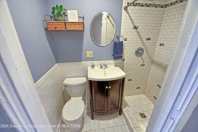 bathroom with toilet, tile walls, tiled shower, vanity, and tile patterned flooring