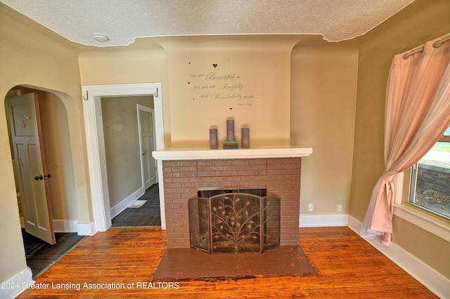 unfurnished living room featuring a textured ceiling, a brick fireplace, and hardwood / wood-style flooring