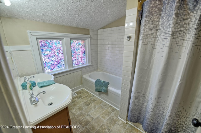 bathroom featuring lofted ceiling, a textured ceiling, tile walls, vanity, and shower / tub combo with curtain