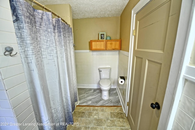 bathroom featuring toilet, a textured ceiling, a shower with curtain, and tile walls