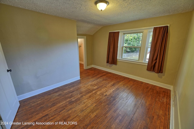 spare room with vaulted ceiling, a textured ceiling, and dark hardwood / wood-style flooring