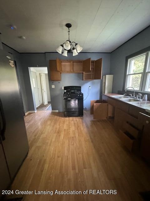 kitchen with sink, black gas range oven, pendant lighting, a notable chandelier, and light hardwood / wood-style flooring