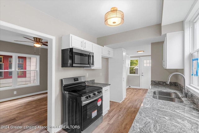 kitchen with light stone counters, white cabinetry, appliances with stainless steel finishes, sink, and light hardwood / wood-style flooring