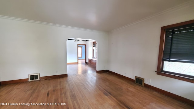 empty room with ornamental molding, wood-type flooring, a wealth of natural light, and ceiling fan