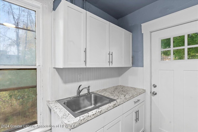 kitchen with light stone countertops, sink, and white cabinets