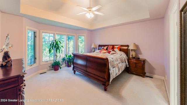 bedroom featuring ceiling fan, light carpet, and a tray ceiling