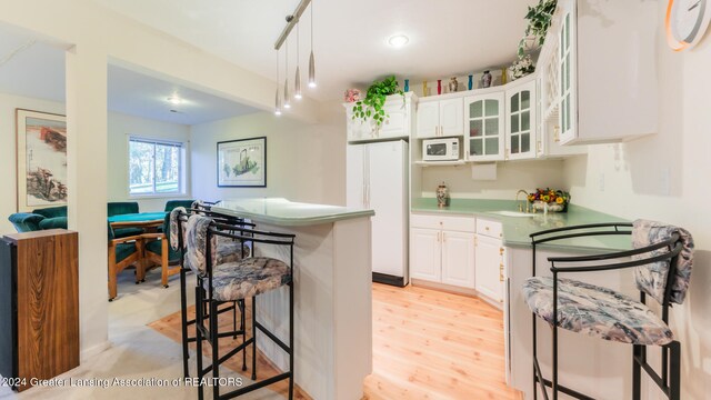 kitchen featuring pendant lighting, white appliances, white cabinets, sink, and a kitchen breakfast bar