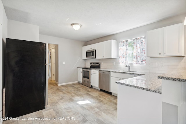 kitchen with backsplash, light hardwood / wood-style flooring, appliances with stainless steel finishes, light stone counters, and white cabinetry