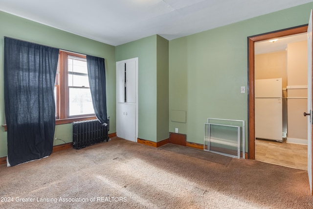 unfurnished bedroom with radiator heating unit, carpet, and white refrigerator