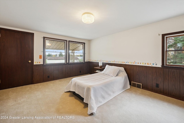 carpeted bedroom featuring wood walls and multiple windows