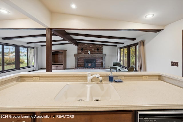 kitchen with stainless steel dishwasher, sink, vaulted ceiling with beams, and a fireplace