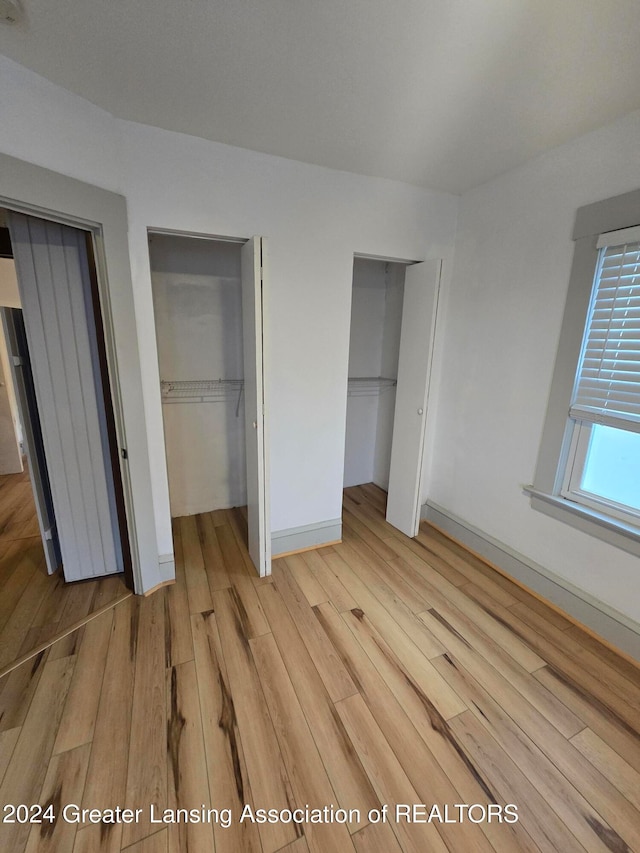 unfurnished bedroom with multiple closets and light hardwood / wood-style floors