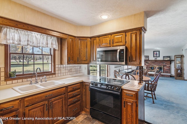 kitchen with sink, kitchen peninsula, a textured ceiling, a fireplace, and black range with electric stovetop