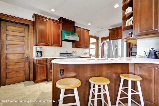 kitchen with light carpet, stainless steel appliances, a breakfast bar area, decorative backsplash, and exhaust hood