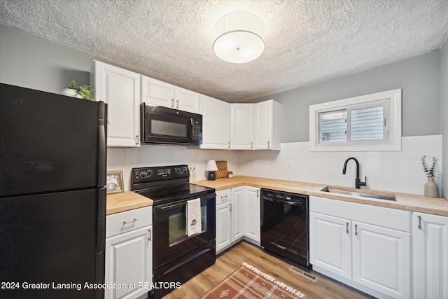 kitchen featuring white cabinets, black appliances, sink, butcher block countertops, and light hardwood / wood-style flooring