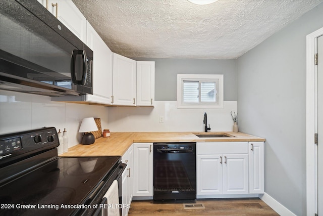 kitchen with butcher block counters, dark wood-type flooring, white cabinets, black appliances, and sink