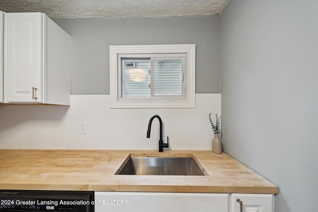 kitchen featuring butcher block counters, sink, a textured ceiling, white cabinets, and dishwasher