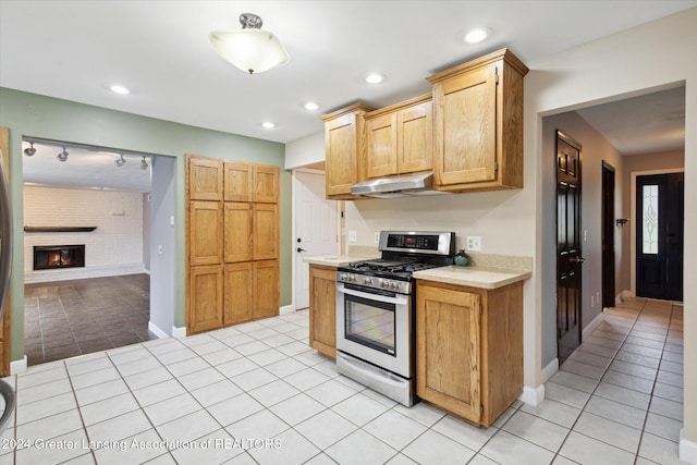 kitchen with stainless steel range with gas cooktop, light tile patterned flooring, and a brick fireplace