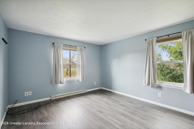 unfurnished room featuring a wealth of natural light, baseboard heating, and light hardwood / wood-style floors