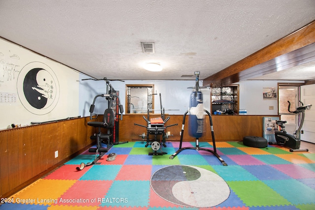 exercise area featuring wood walls and a textured ceiling