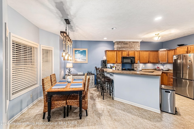 kitchen with decorative light fixtures, stainless steel refrigerator, a textured ceiling, sink, and a breakfast bar area