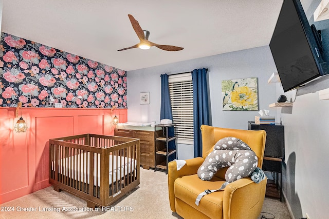 bedroom with a crib, light carpet, and ceiling fan