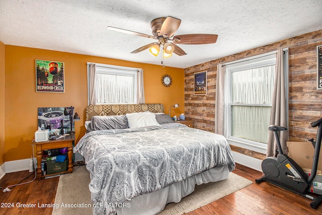 bedroom with hardwood / wood-style floors, ceiling fan, wood walls, and a textured ceiling