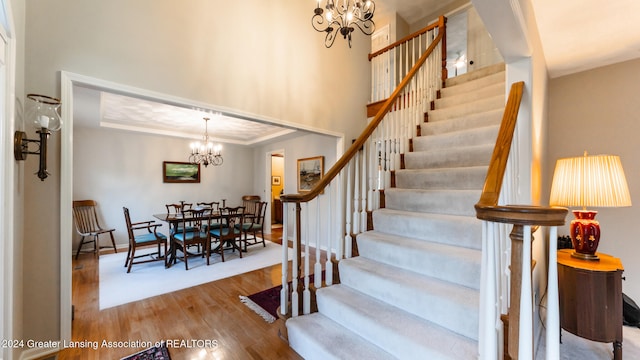 stairs featuring wood-type flooring, an inviting chandelier, and a tray ceiling