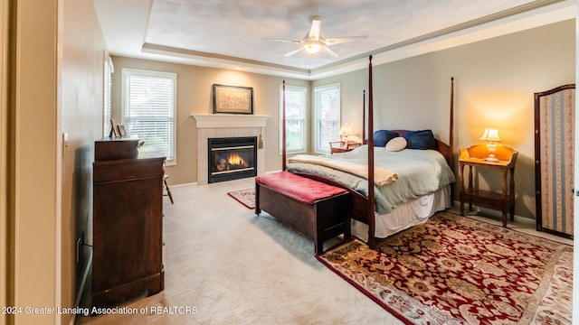 carpeted bedroom featuring ceiling fan, a tiled fireplace, and a tray ceiling