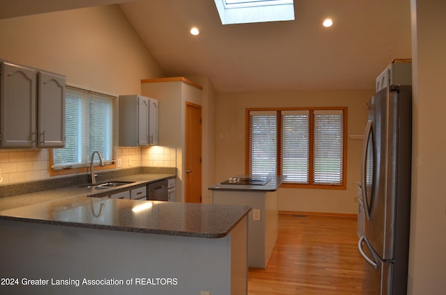 kitchen with a skylight, sink, stainless steel appliances, kitchen peninsula, and decorative backsplash