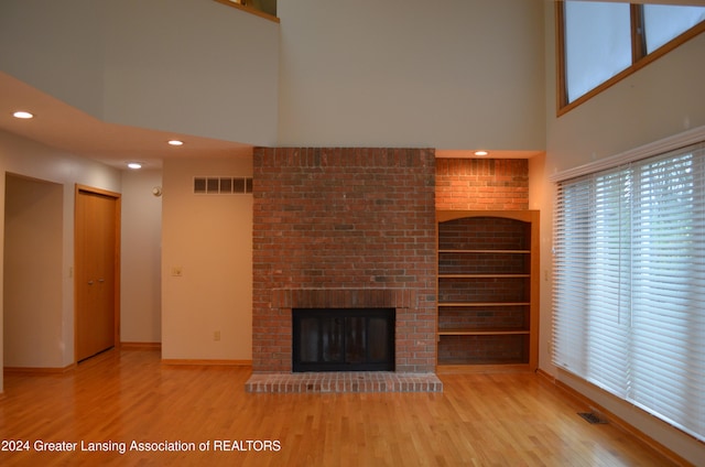 unfurnished living room with built in shelves, light hardwood / wood-style floors, a high ceiling, and a brick fireplace