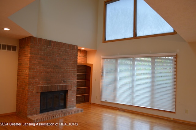 unfurnished living room featuring light wood-type flooring, built in features, a fireplace, and a high ceiling