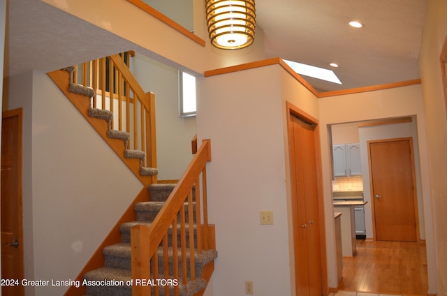 staircase featuring hardwood / wood-style floors, crown molding, and a skylight