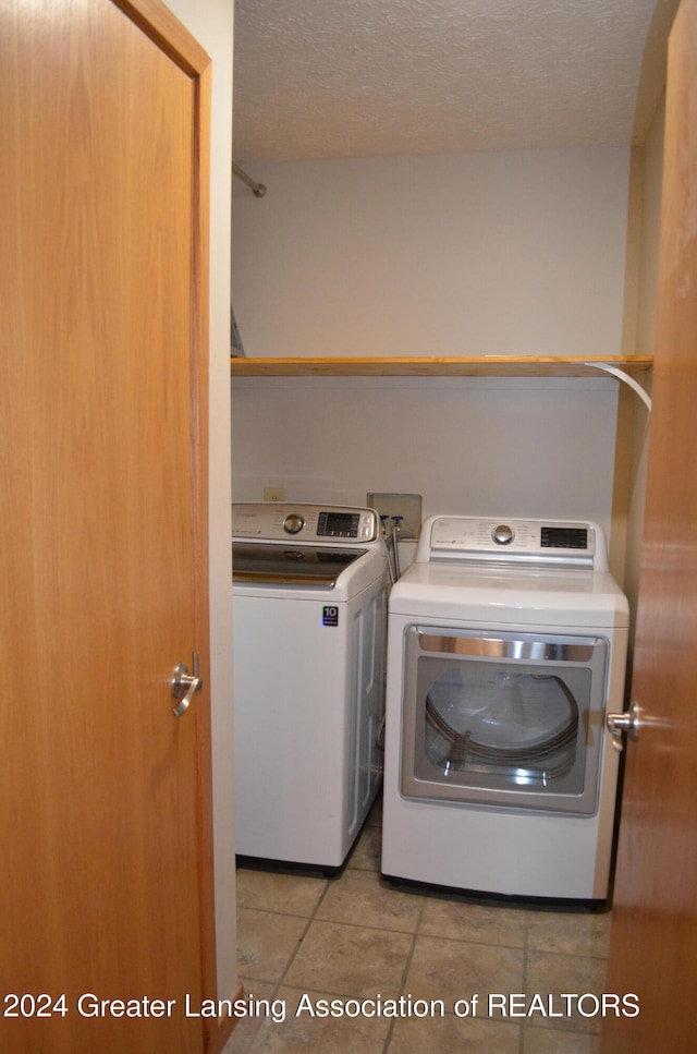 clothes washing area featuring washing machine and dryer, light tile patterned floors, and a textured ceiling