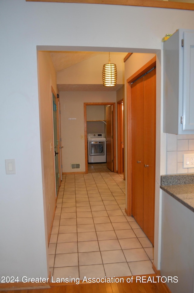 hall with a barn door, washer / clothes dryer, light tile patterned floors, and vaulted ceiling