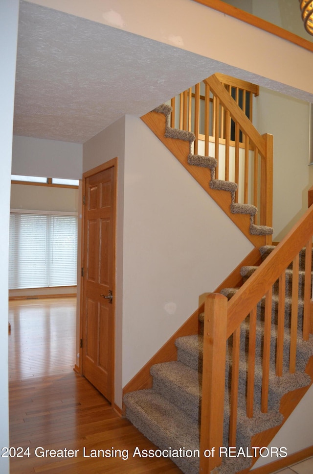 stairs with wood-type flooring and a textured ceiling