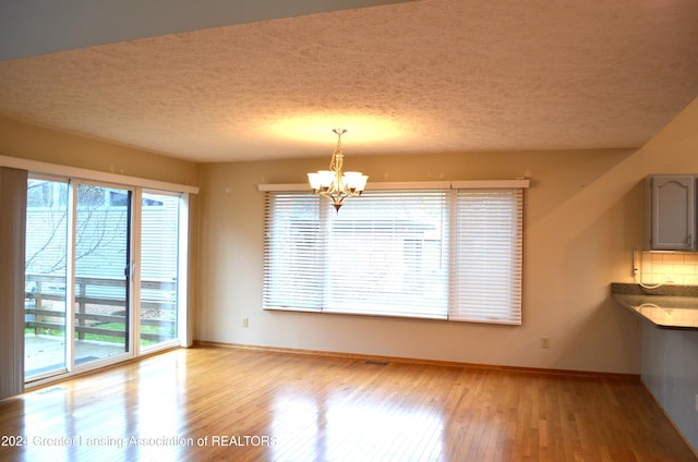 unfurnished dining area with a notable chandelier, a healthy amount of sunlight, and light wood-type flooring