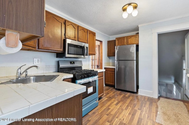 kitchen featuring tile counters, dark hardwood / wood-style flooring, a textured ceiling, sink, and appliances with stainless steel finishes