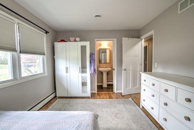 bedroom featuring baseboard heating, light wood-type flooring, ensuite bath, and sink