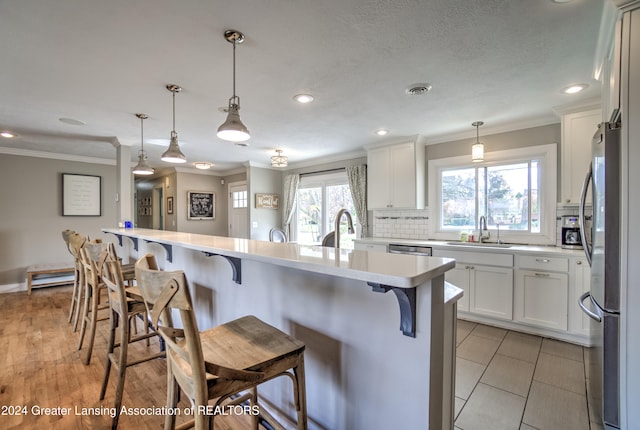 kitchen with sink, stainless steel refrigerator, a kitchen breakfast bar, and white cabinets