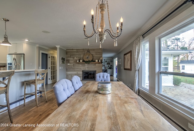 dining area with hardwood / wood-style floors, a fireplace, an inviting chandelier, and crown molding