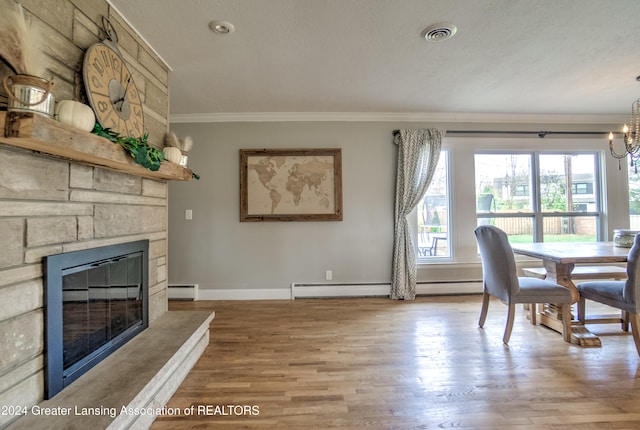 dining room featuring baseboard heating, a textured ceiling, a fireplace, light hardwood / wood-style flooring, and crown molding