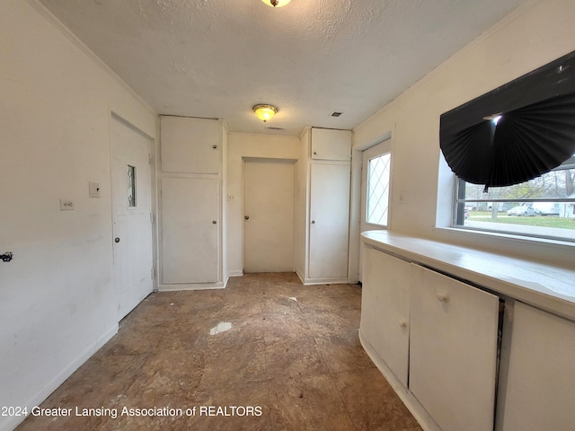 interior space featuring white cabinetry, a textured ceiling, and ornamental molding