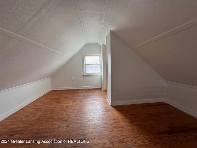 additional living space with hardwood / wood-style flooring, a textured ceiling, and vaulted ceiling