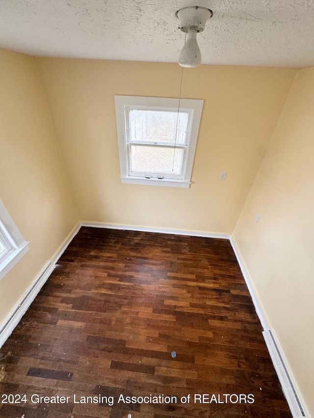 unfurnished dining area featuring a textured ceiling, a baseboard radiator, and dark hardwood / wood-style floors